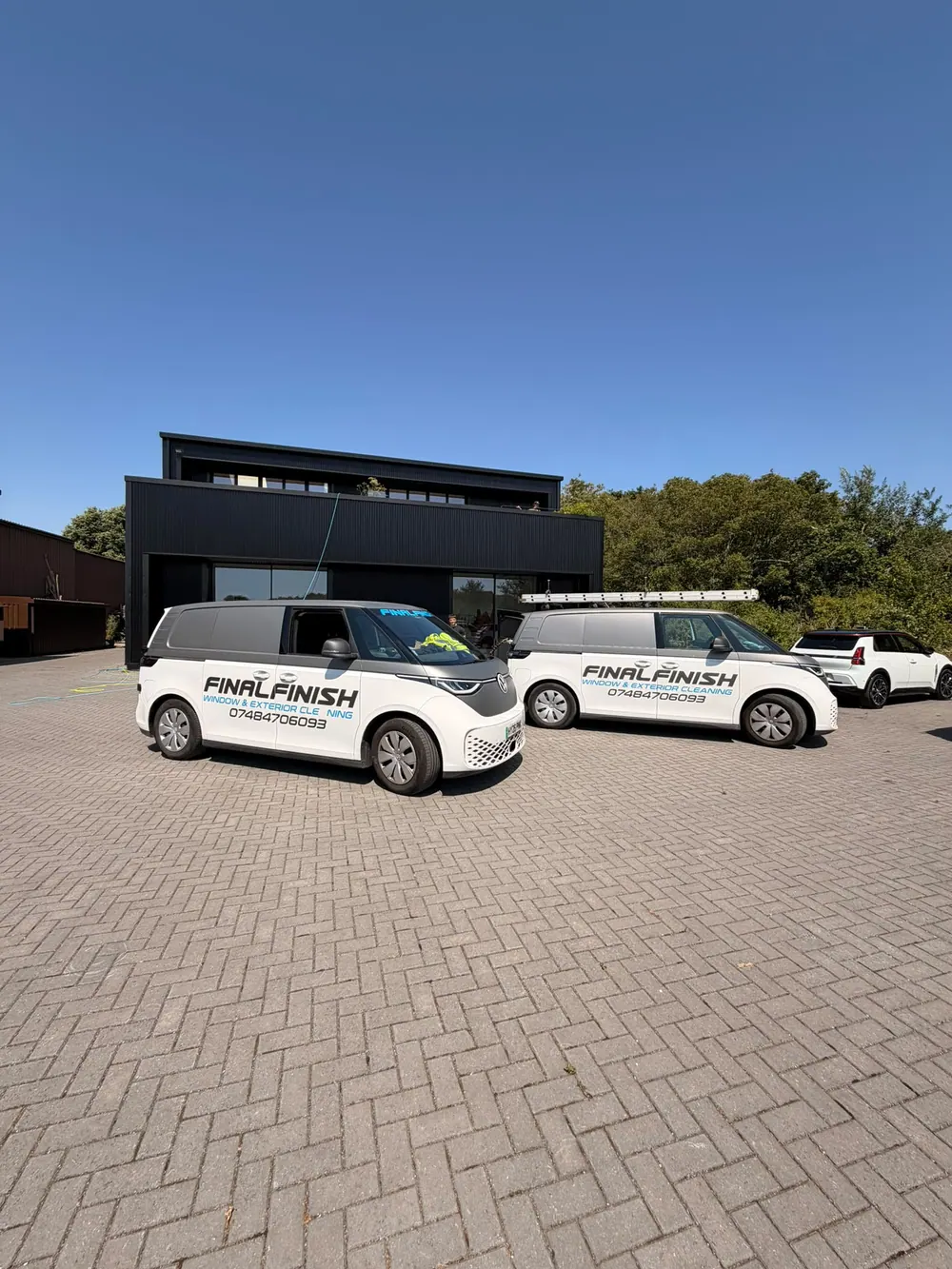 Two Final Finish vans parked outside a modern black timber-clad house